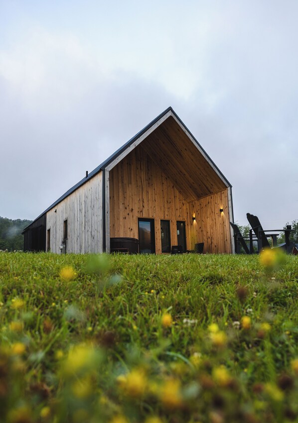 A wooden barn with a sloped roof, large doors, and two windows on the front.