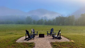Ett lugnt utomhusområde med fyra Adirondack-stolar och ett litet bord, omgivet av en grusbelagd cirkel på en gräsyta med ett berg i bakgrunden.