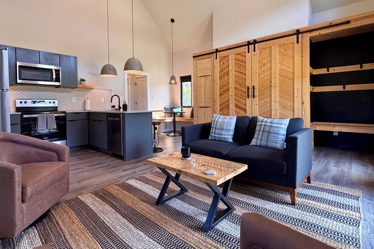 Een moderne keuken met een magnetron, oven en een bar met barkrukken. In de woonkamer staat een bank en een bijzettafeltje.