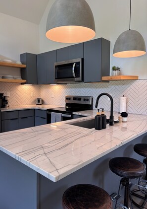 A modern kitchen with a large island, dark cabinetry, and pendant lighting.