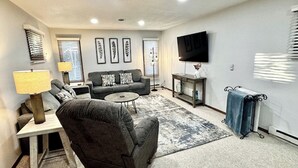 A living room with a sofa, armchair, coffee table, and a TV on a stand. - 3-bedroom house in delightful Mapleton with AC, WiFi. Unwind and enjoy! (Mapleton)