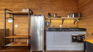 A compact kitchen with a stainless steel refrigerator, a built-in oven, and a coffee maker on a wooden shelf. - Cabana c\ lareira prox. de Florianópolis VST033 (Anitapolis)