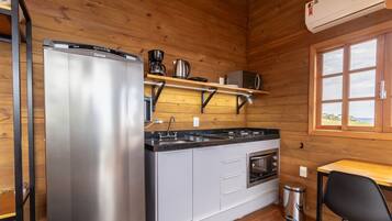 Cocina compacta con refrigerador, estufa, horno y cafetera sobre una repisa.