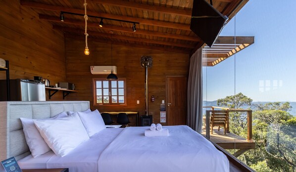 Un dormitorio de cabaña de madera con una cama, un escritorio, una estufa y vistas al exterior.