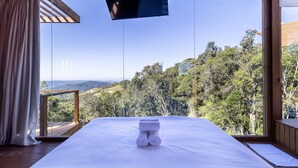 A bedroom with a large window offering a view of a forested landscape. - Cabana c\ lareira prox. de Florianópolis VST033 (Anitapolis)