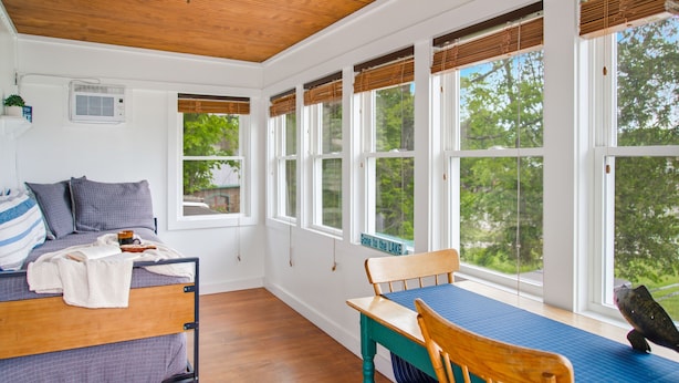 A room with a bed, a table, and large windows.