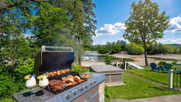 A barbecue grill with food, a pool, and outdoor seating.