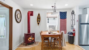 A kitchen with a wood-burning stove, a dining table with chairs, a refrigerator, and an American flag.