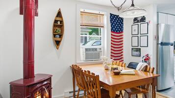 A dining area with a wooden table, chairs, a red wood stove, an American flag, and a refrigerator.