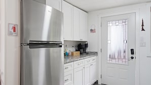 A kitchen with white cabinets, a stainless steel refrigerator, a coffee maker, and a door with a frosted glass panel.