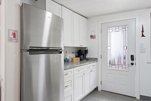 A kitchen with white cabinets, a stainless steel refrigerator, a coffee maker, and a door with a frosted glass panel. - Hot Tub, 5 min to Colgate, Sleeps 6, Welcome Wine (Madison)