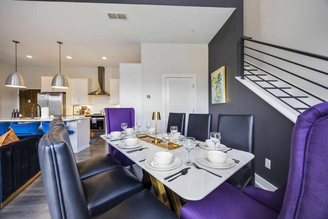Un espace de salle à manger moderne, avec une longue table dressée pour quatre personnes, entour ée de chaises à revêtement violet.