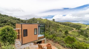 Une cabane moderne et compacte, dotée de grandes fenêtres, située sur une colline et offrant une vue panoramique sur le paysage environnant.