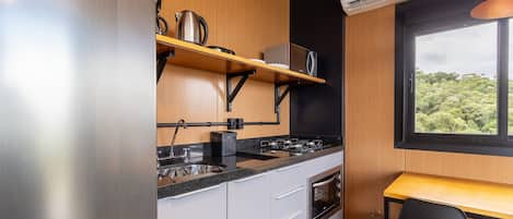 A compact kitchen with a built-in stove, oven, and microwave, a small sink, and a window overlooking greenery.