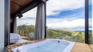 Un balcón con jacuzzi, terraza de madera y vistas a colinas verdes.