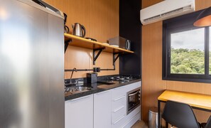 Une cuisine compacte dotée d’appareils électroménagers en acier inoxydable, d’un plan de travail en bois et d’une fenêtre donnant sur un paysage verdoyant.
