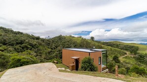 Un edificio moderno de un piso con techo plano, ubicado en una ladera con abundante vegetación.
