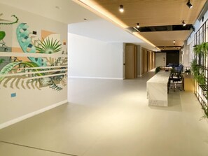 A modern office space with a long reception desk, a mural with abstract designs, and a plant wall. - Studio Shopping OKA Floripa - SOK116 (Florianopolis)