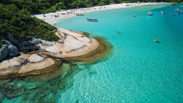 A coastal beach with clear turquoise waters, rocky formations, and dense greenery. - Studio Shopping OKA Floripa - SOK116 (Florianopolis)