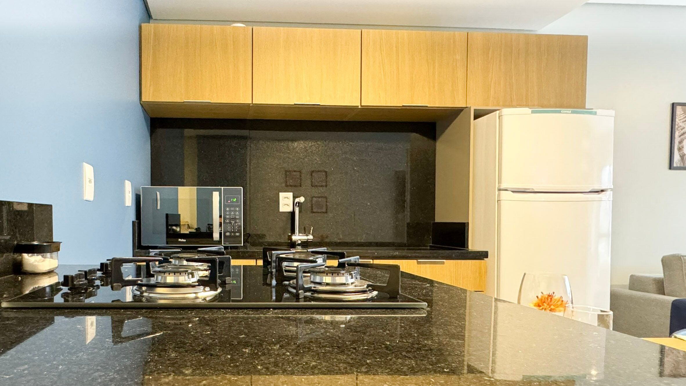 Una cocina moderna con encimera negra, microondas integrado, estufa y refrigerador blanco.