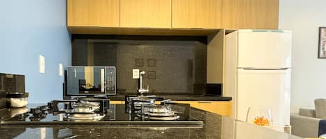 Una cocina moderna con encimera negra, microondas integrado, estufa y refrigerador blanco.