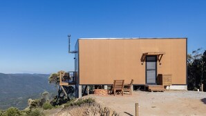A modern building with a flat roof, a small porch with a bench, and a view of the surrounding landscape.