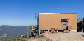 Ein modernes Gebäude mit flachem Dach, einer kleinen Veranda mit Holzmöbeln und freiem Blick auf die umliegende Landschaft.