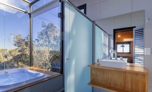 Une salle de bain moderne dotée d’une grande fenêtre, d’un jacuzzi et d’un meuble-lavabo en bois.