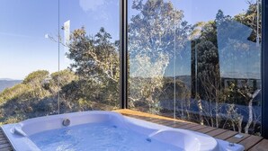 Un jacuzzi en una terraza de madera con vista despejada a árboles y colinas al fondo.