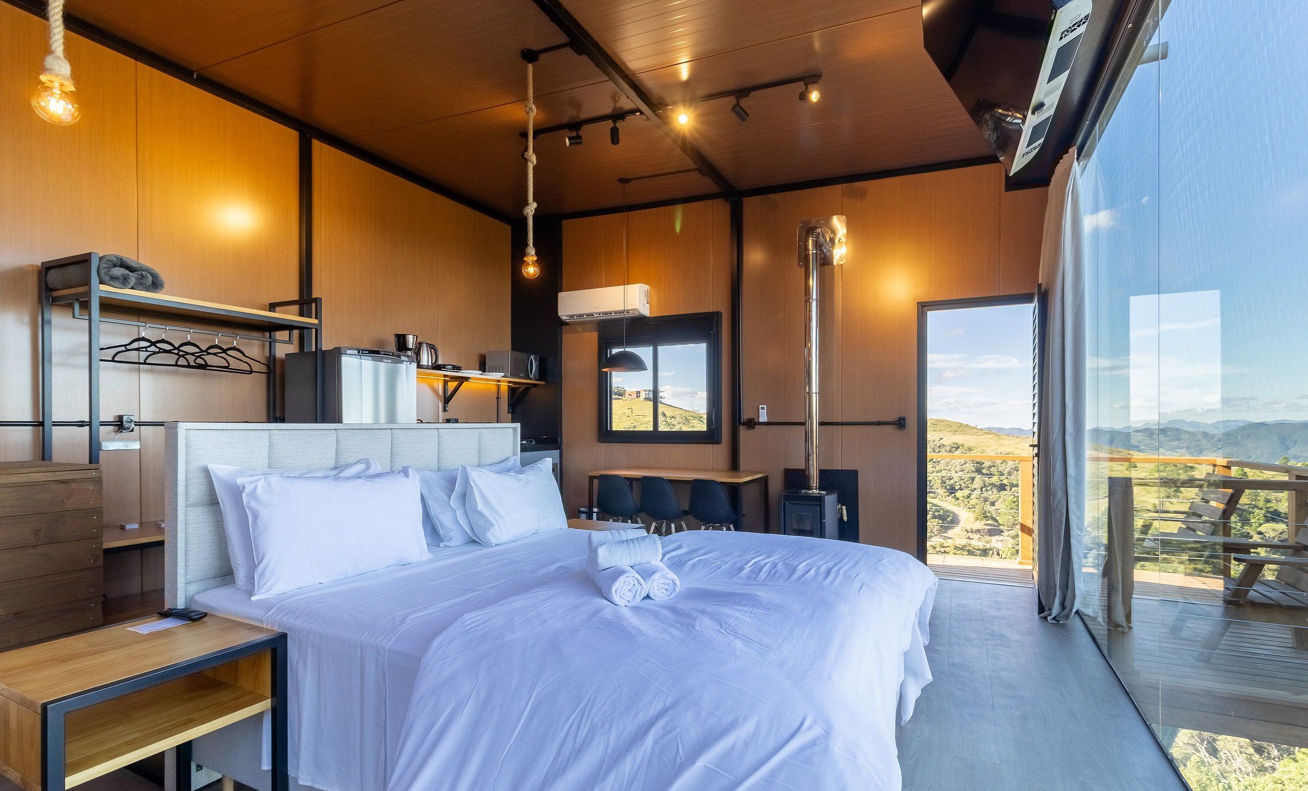 A modern bedroom with a large bed, a desk, and a view of the outdoors.
