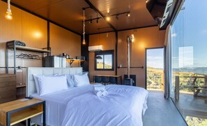 A modern bedroom with a large bed, a desk, and a view of the outdoors.