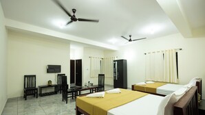A hotel room with two beds, a TV, a desk, chairs, and ceiling fans. - Golden Crest Residences (Madikeri)