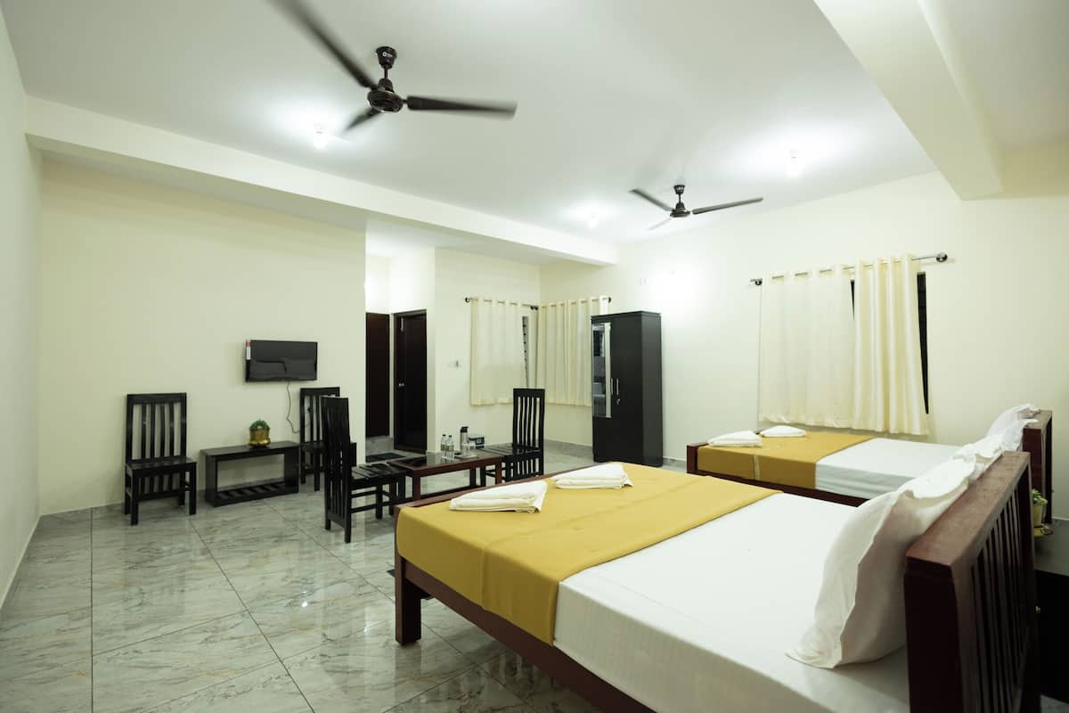 Quarto de hotel com duas camas, televisão, escrivaninha, cadeiras e ventiladores de teto.