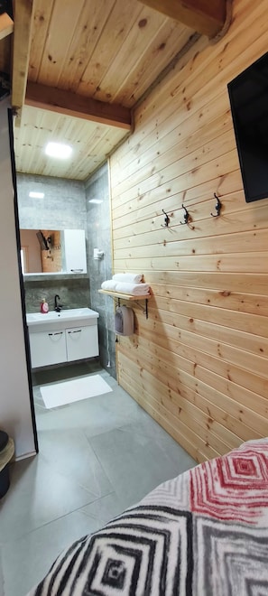 A bedroom with a wooden ceiling, a bed with a patterned blanket, a bedside table, and a wall-mounted heater. - YeşilKöy Pansiyon (Çamlıhemşin)