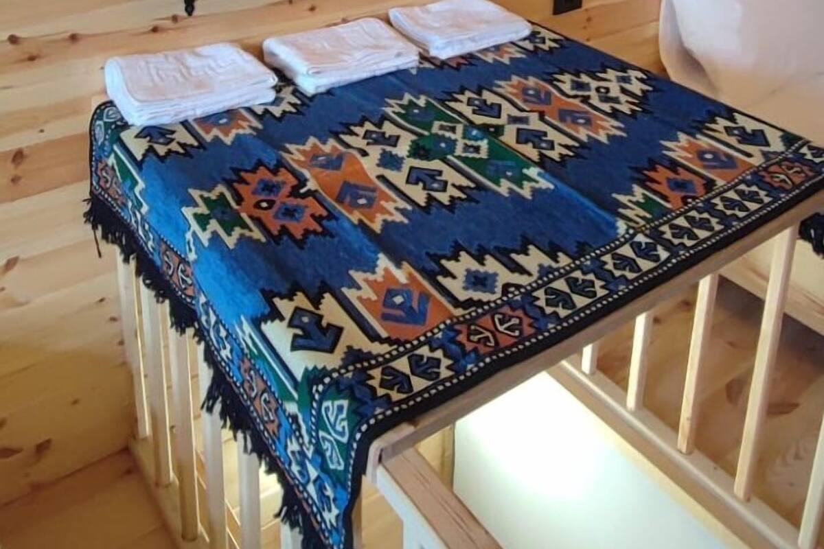 A wooden cabin interior with a bed, a colorful rug, and neatly stacked towels on shelves.