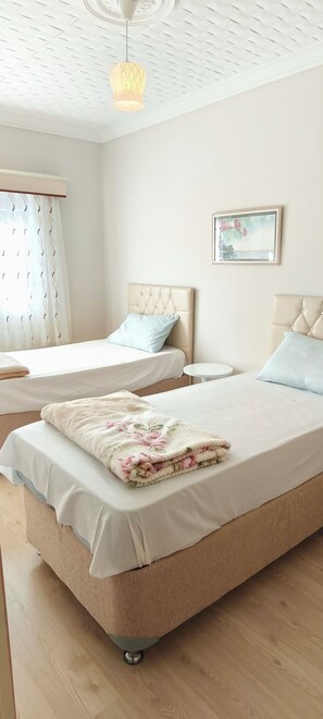A hotel room with two beds, a round table, a painting on the wall, and a ceiling light fixture. - YeşilKöy Pansiyon (Çamlıhemşin)