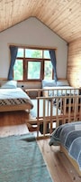 A room with a sloped ceiling, wooden walls, a large window with curtains, two beds, and a view of greenery outside.