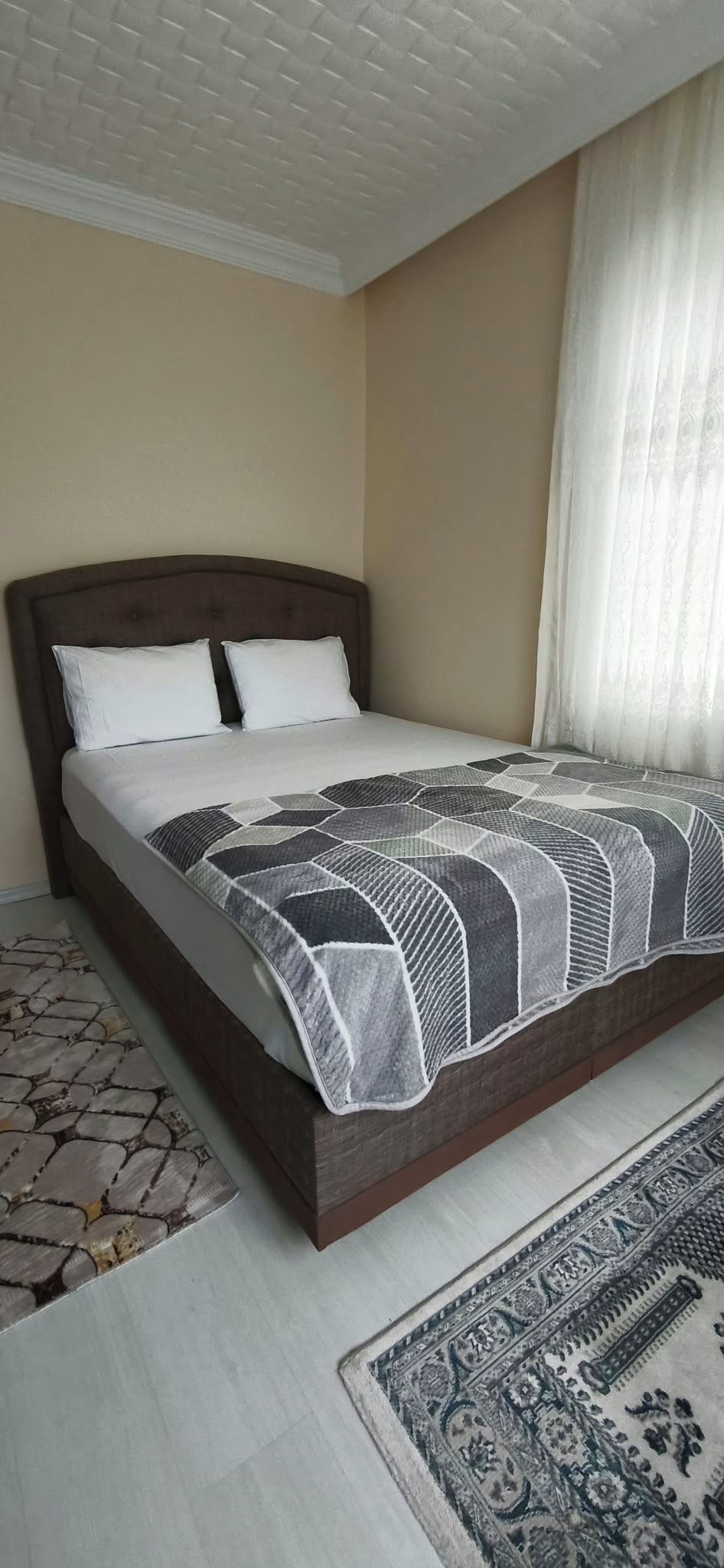 A bedroom with a bed, a patterned rug, and a window with curtains.