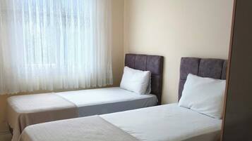 A hotel room with two beds, a window with sheer curtains, a ceiling fan, and a patterned rug.