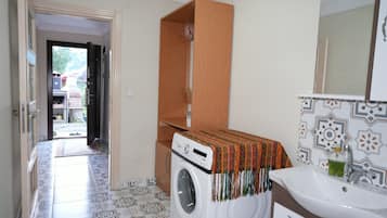 A compact bathroom with a washing machine, a sink, and a mirror.