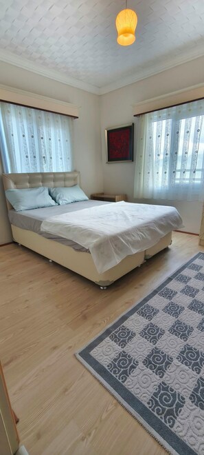 Un dormitorio con una cama grande, una mesita de noche, una lámpara colgante y una alfombra estampada.