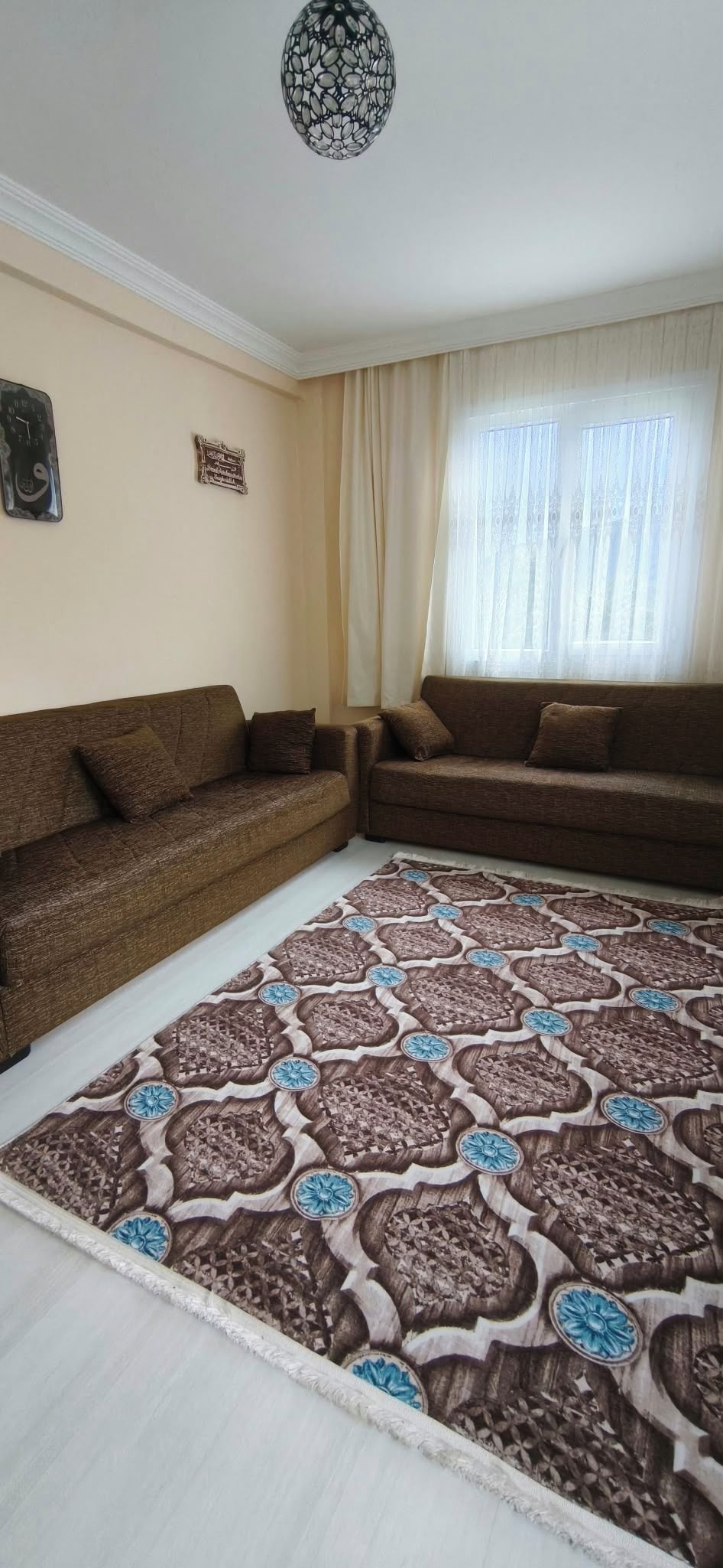 Una sala de estar con dos sofás, un tapete estampado, un reloj de pared y una lámpara decorativa en el techo.