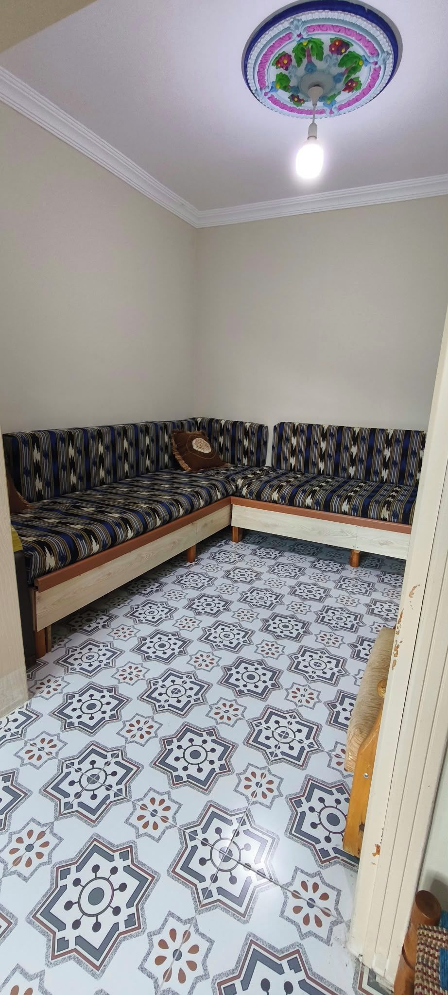 Ett rum med en hörndelad soffa, mönstrade golvplattor och en dekorativ taklampa.