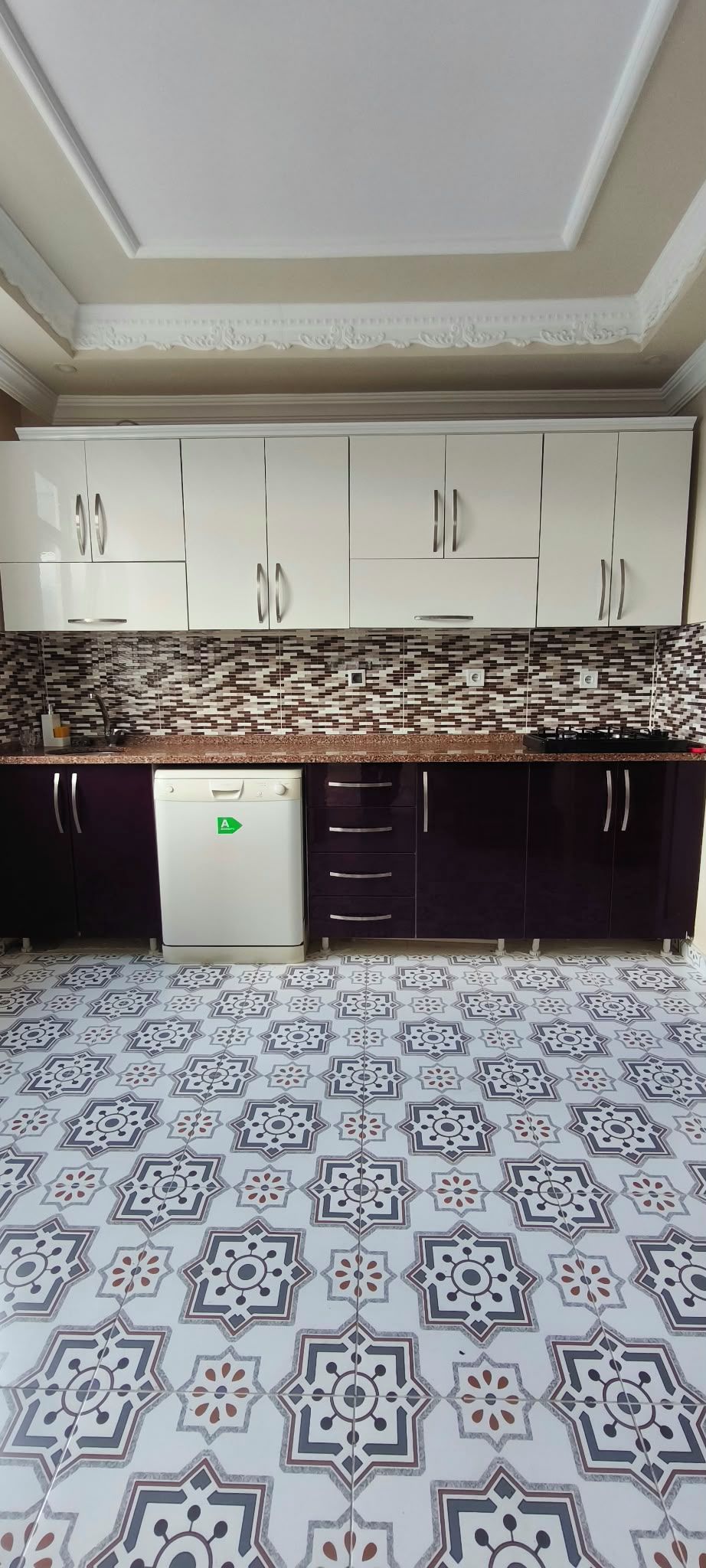 A kitchen with white cabinets, a patterned backsplash, and a tiled floor.