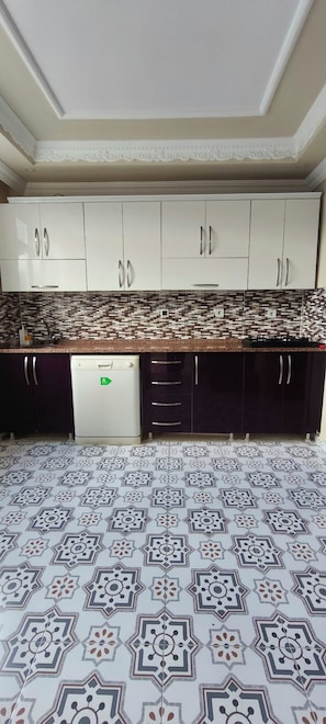 Una cocina con armarios blancos, un salpicadero estampado y suelo de baldosas.