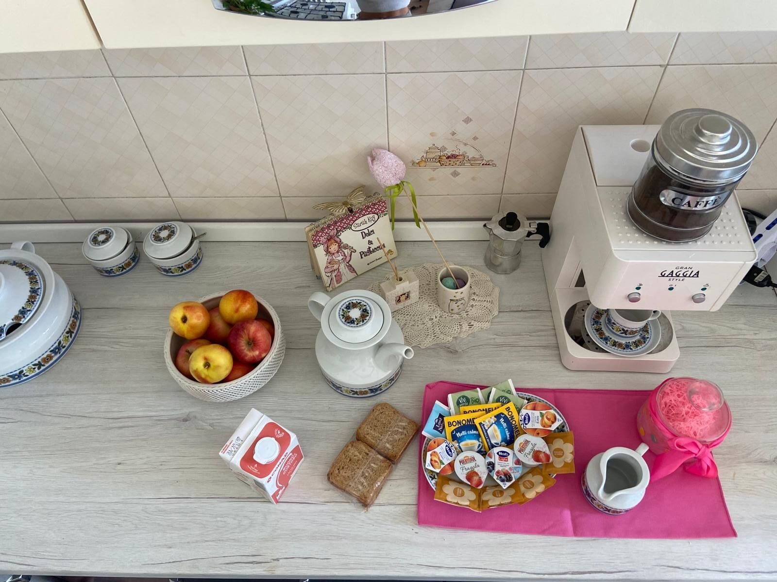 A kitchen counter with a coffee maker, teapot, fruit bowl, bread, and various food items.