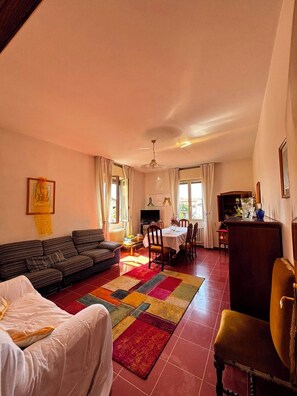 A living room with a sofa, a dining table, and chairs. There is a television and a radiator. - Elisa Maison (Santa Maria degli Angeli)