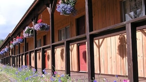 A wooden building with multiple windows and doors, some with red frames. There are hanging flower baskets on the exterior.
