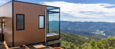 A modern cabin with a hot tub, wooden furniture, and a scenic mountain view.