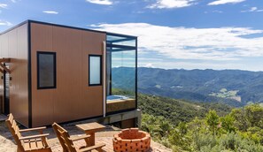 A modern cabin with a glass wall offering a mountain view, a wooden deck with seating, and a hot tub. - Cabana romântica perto de Florianópolis VST038 (Anitápolis)